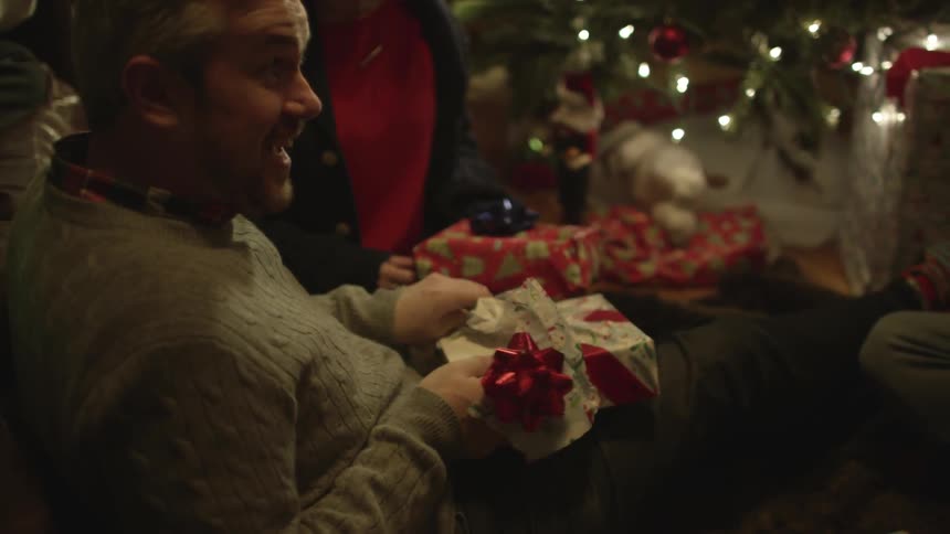 Several people watch as a man opens a christmas gift