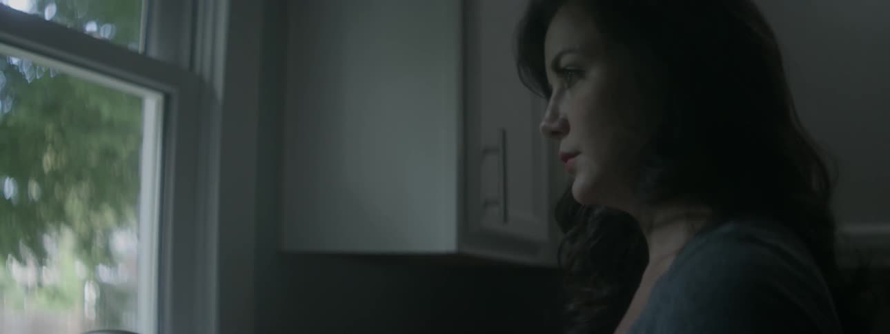 A woman stops doing dishes in a kitchen and stares out of the window