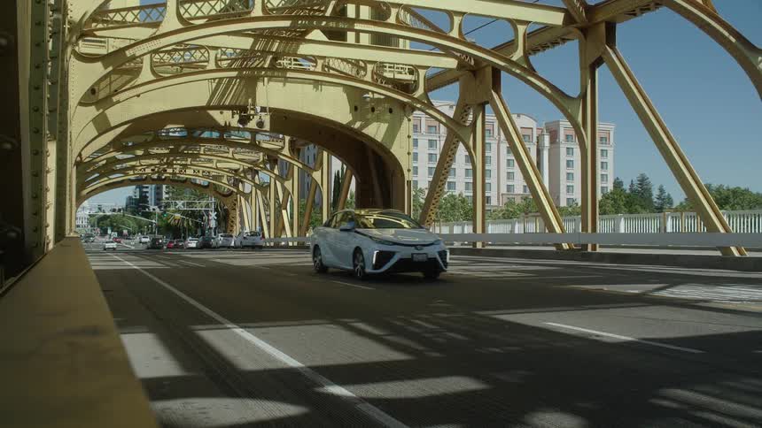 A car is driving over an metal bridge leading out of a city
