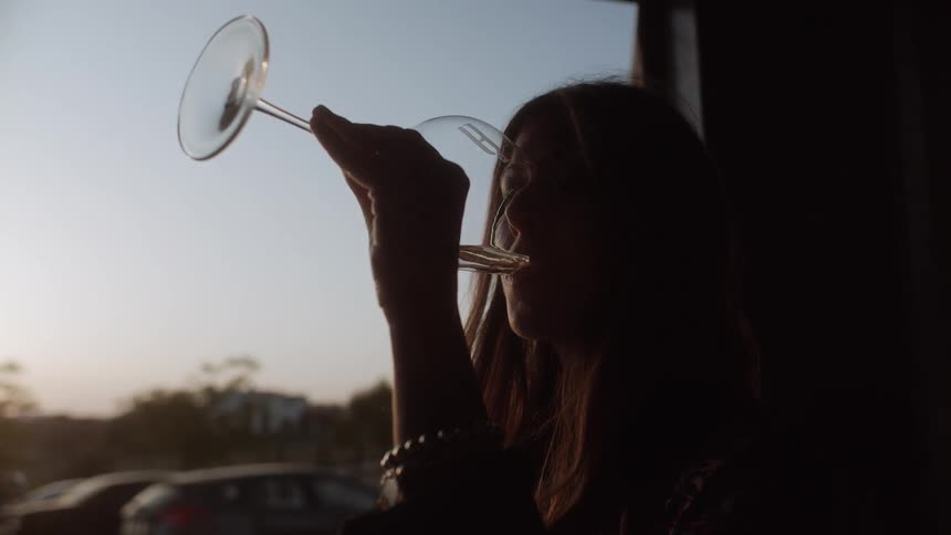 Woman drinks from a wine glass at sunset