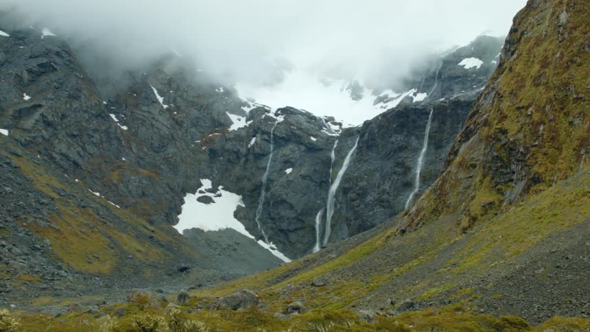Waterfalls cascade down a ravine on a mountainside on a cloudy day