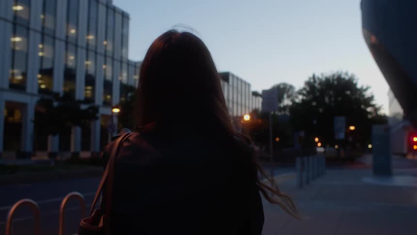 A woman is walking on a city sidewalk at dusk