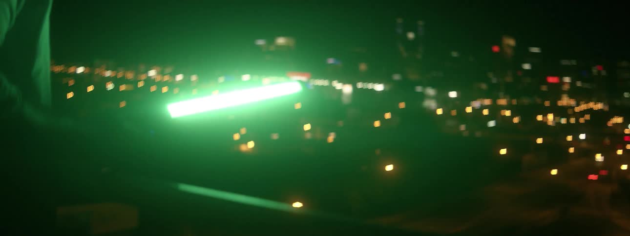 A man holds a light as he stands on a roof overlooking a city at night