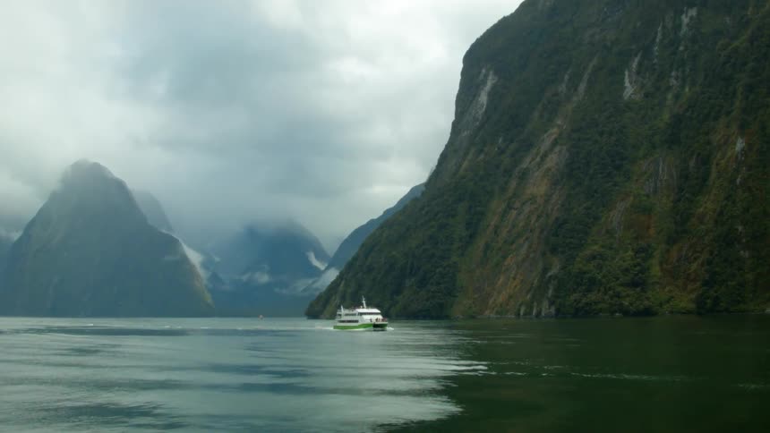 A passenger boat travels past a mountainous coastline on a cold day