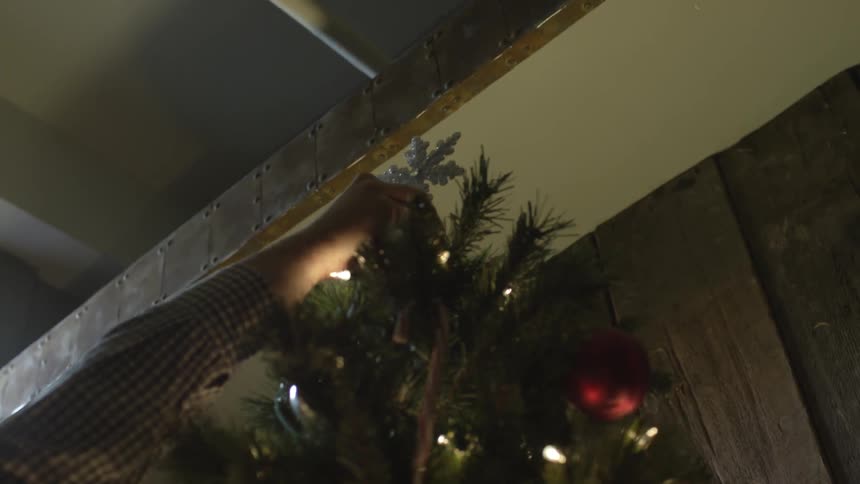 A white puts a snowflake decoration on top of a christmas tree