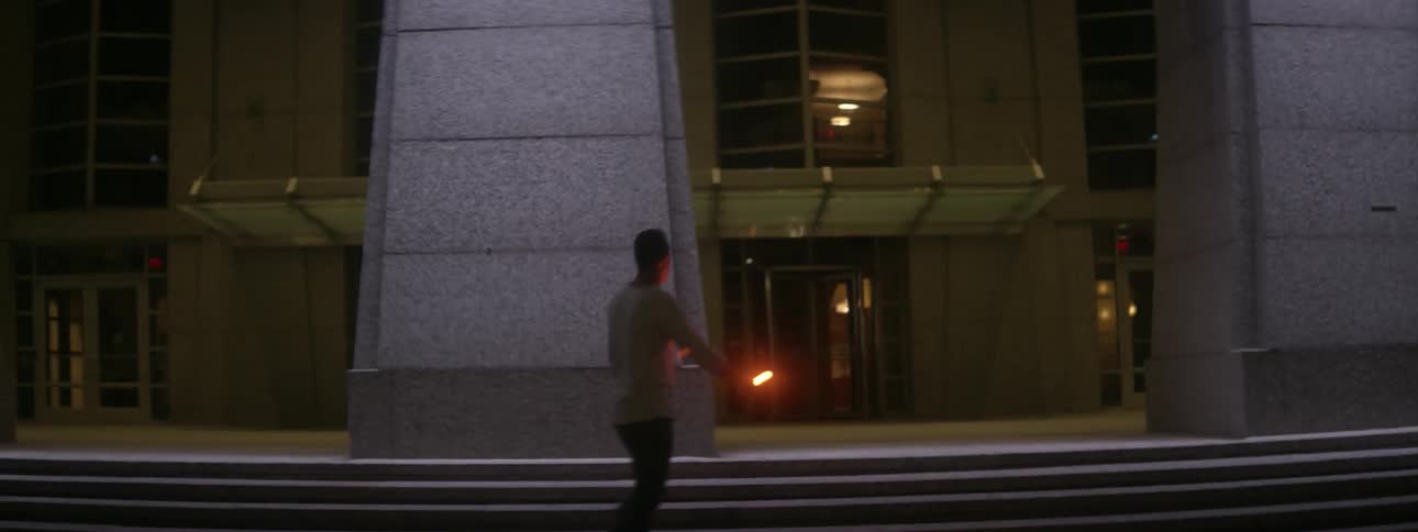 Man with glow stick walks in front of building at dusk