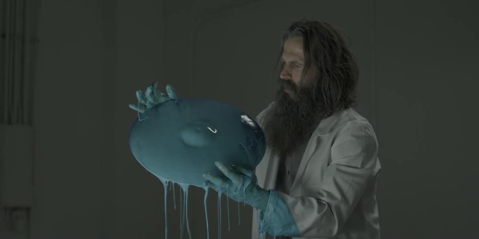 Man wearing gloves lifts a round blue object that is dripping with paint