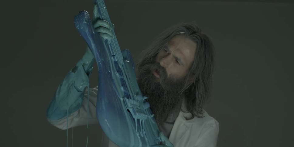 A man in a lab coat is pulling a guitar out of a blue liquid