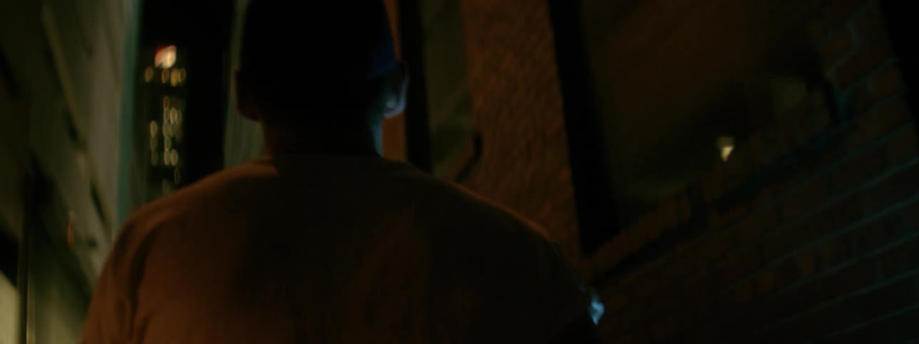 A man carries a flashlight down a dark alley