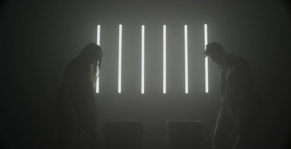 Two drummers beat drums in a dim room