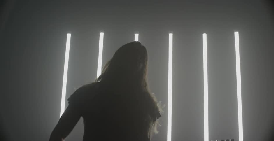 A person is playing a guitar in a dark room with a slatted window