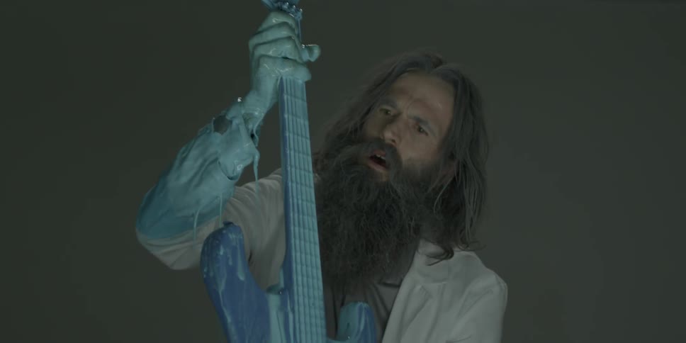A bearded man dips a guitar in blue paint