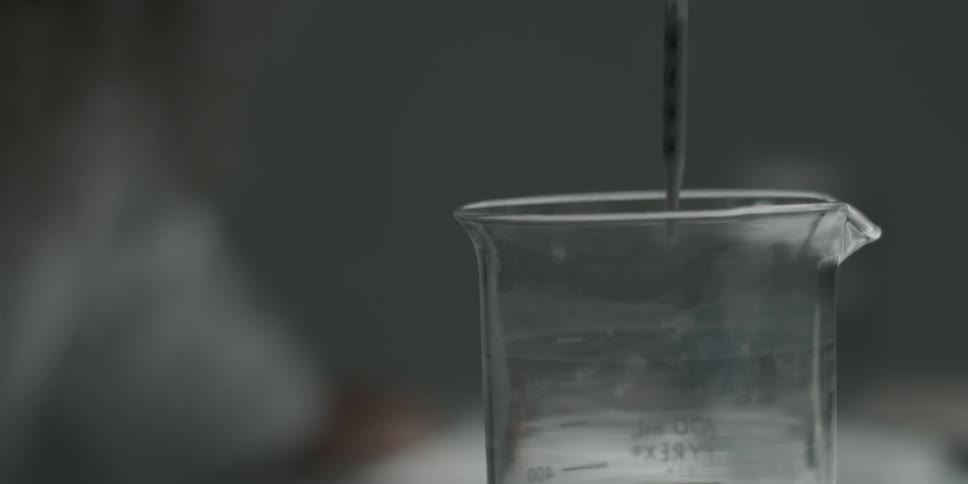 A man drips liquid into a beaker glass