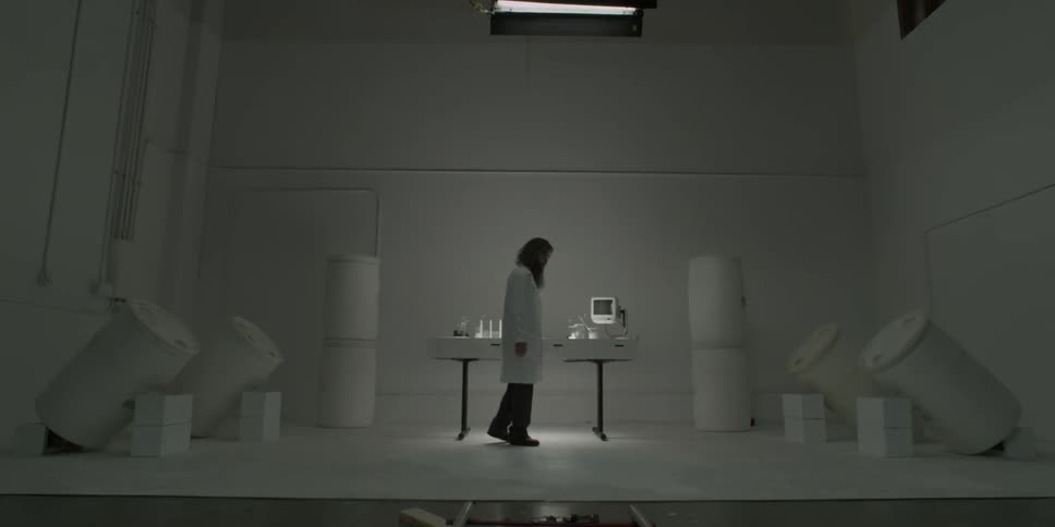 A man with long hair and beard in a lab coat turns to face a table