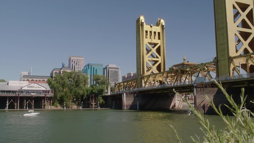 A boat is going up a river toward a bridge on a sunny day