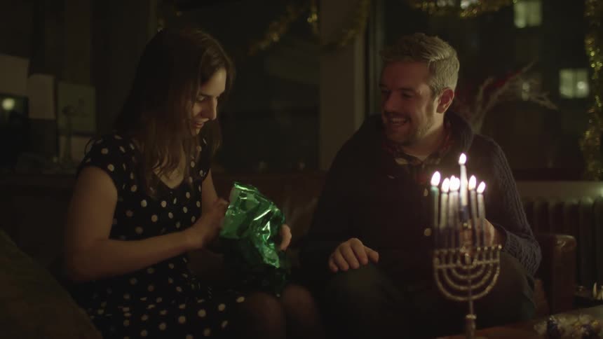 A woman opens a gift in front of a burning menorah