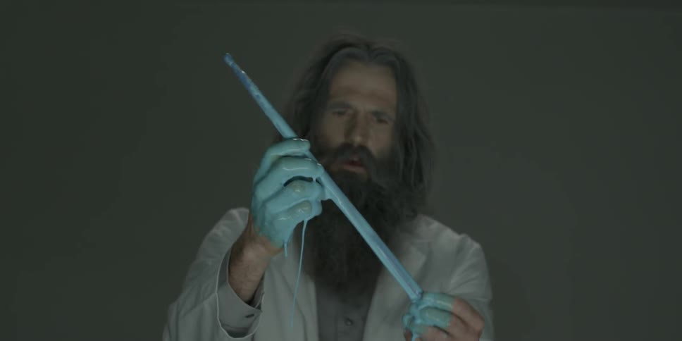 A scientist is pulling a drumstick from some blue liquid and examining it