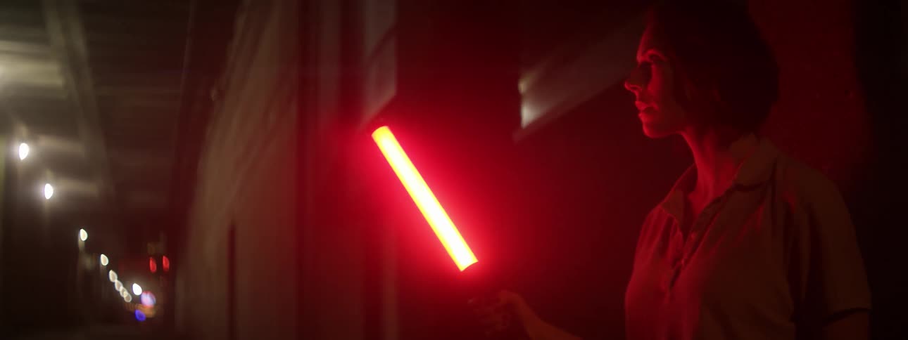 A woman carries a red flashlight outside at night