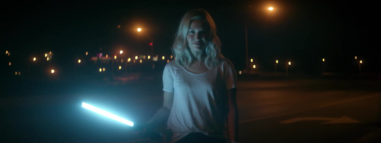 Woman holds a glowing lightsaber in a city at night