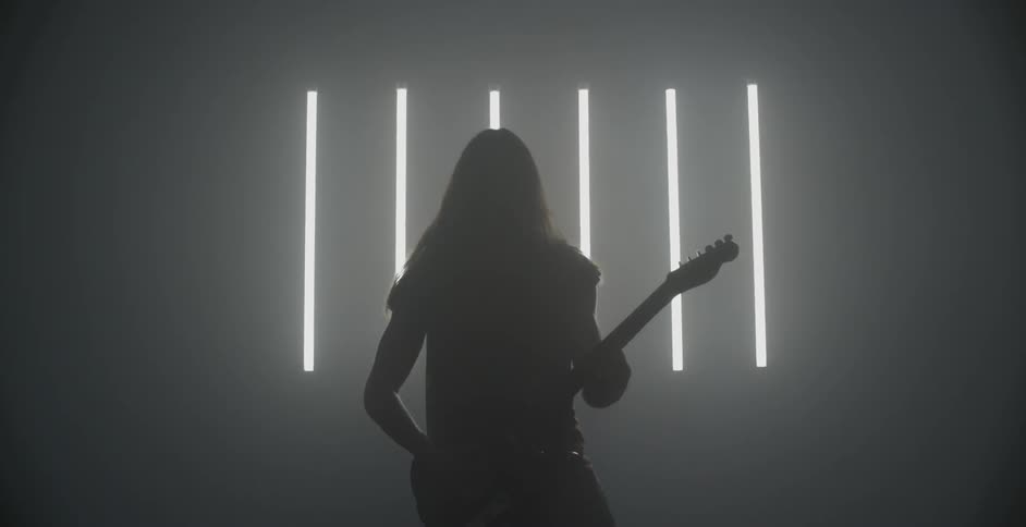 A person is playing a guitar in a dark room with a slatted window