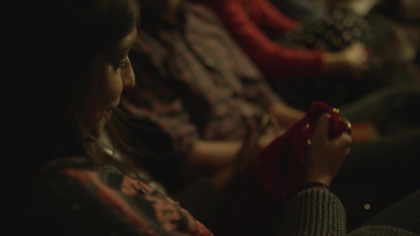 A woman opens a christmas gift at a gathering of friends