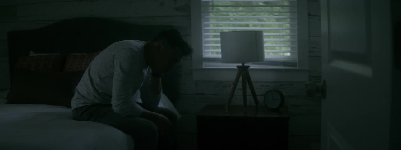 A man takes a deep breath as he sits on the edge of his bed
