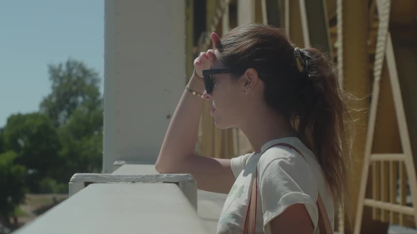 A woman leans on a bridge railing and looks out