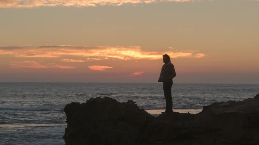 Man looks out at the water at sunset
