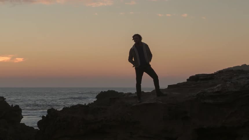 A man stands atop a shore side cliff