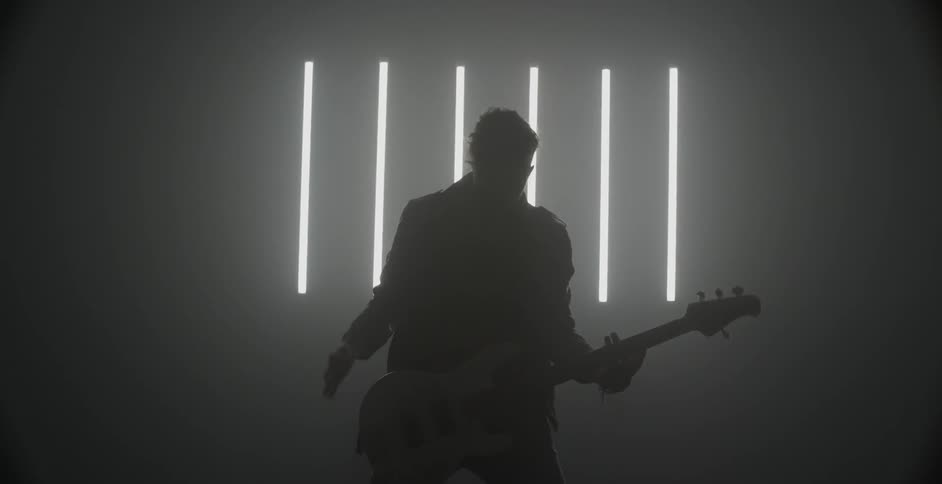 A bassist plays and dances in a dim room