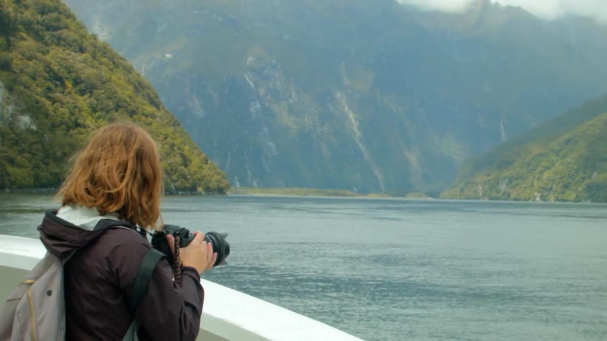A woman is taking photos of a mountainous coastline from a ship