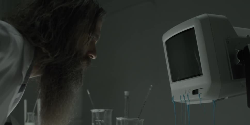 A bearded man stares intently at a screen leaking blue fluid