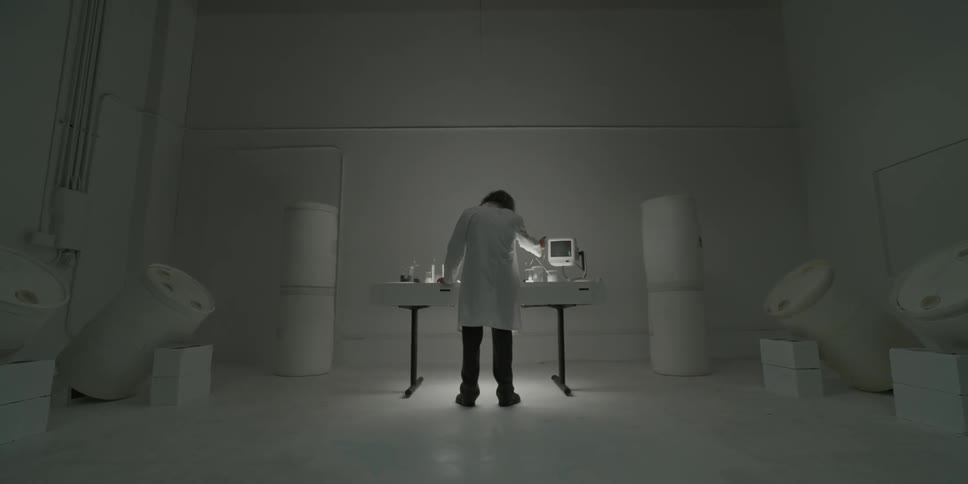 A man in a lab coat is fiddling with various bits of lab equipment on a table in a room
