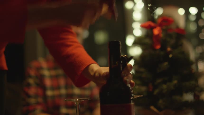 Person uncorks a bottle as others sit around a christmas decorated area