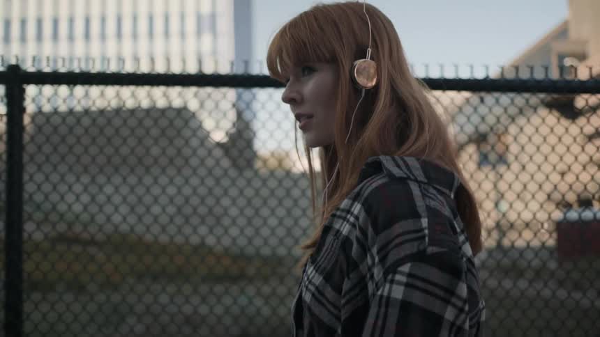 A woman wearing earphones drags her hand along a fence as she walks