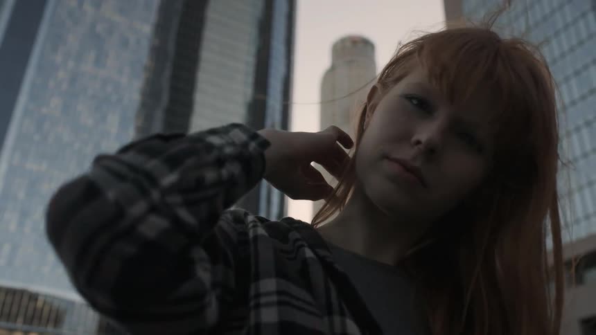 Woman brushes her hair back standing in front of tall buildings