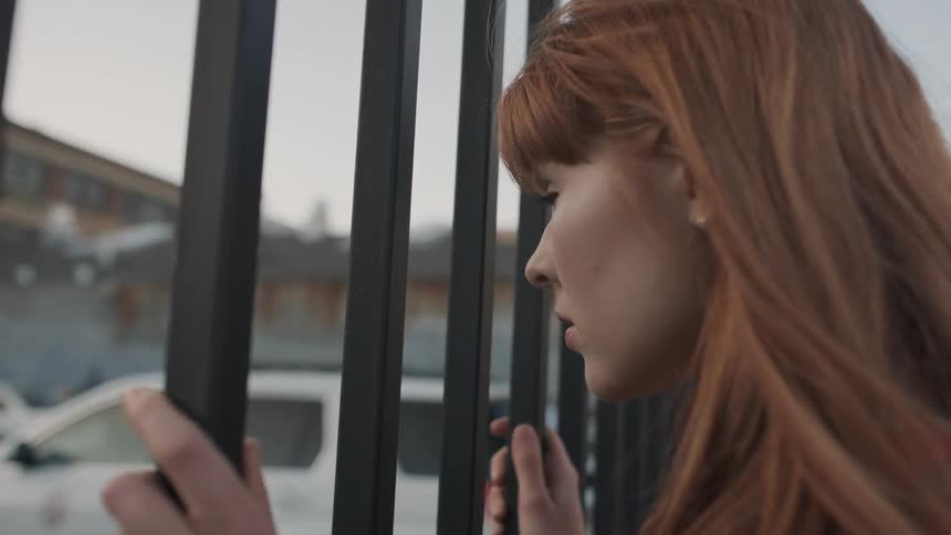 A red haired woman stands by a black fence
