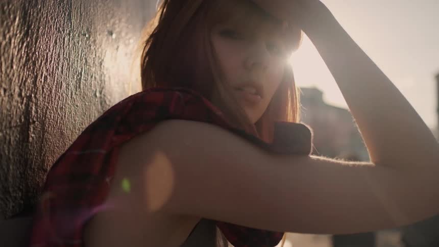 A red haired woman leans against a concrete wall