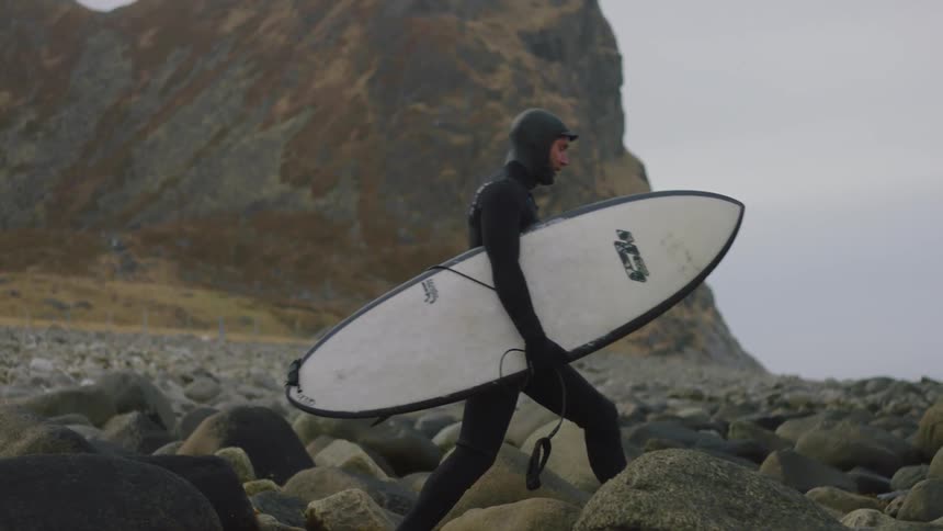 A man carries a surfboard over the rocks