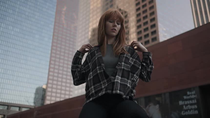 A woman sitting on a wall in a city is adjusting her shirt