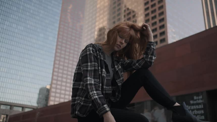 A woman sitting on a wall in the city is playing with her hair