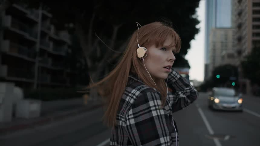 A red haired woman crosses the street while wearing headphones
