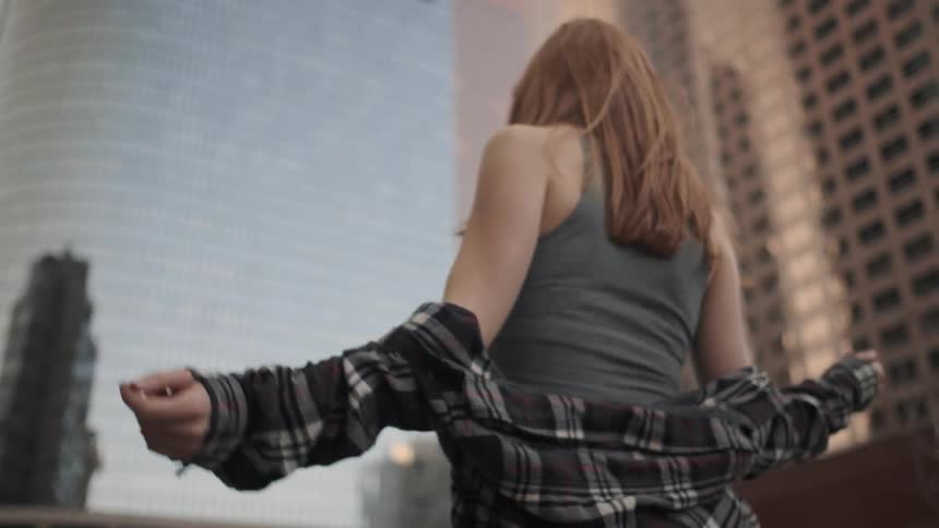A woman pulls her shirt on over her shoulders as she walks in a city during the day
