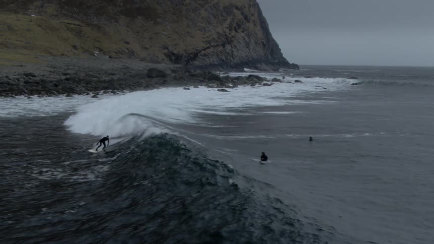 A surfer catches a wave at a beach on a rugged coast