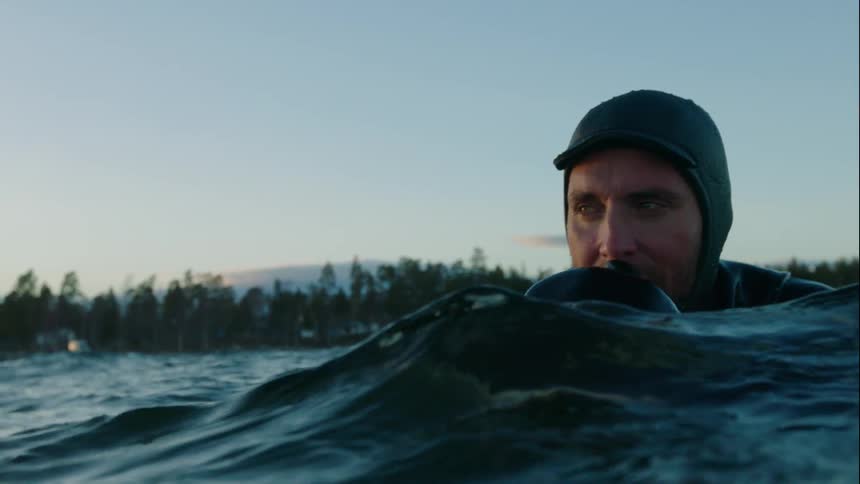A man in a wetsuit floats in the water on a surfboard