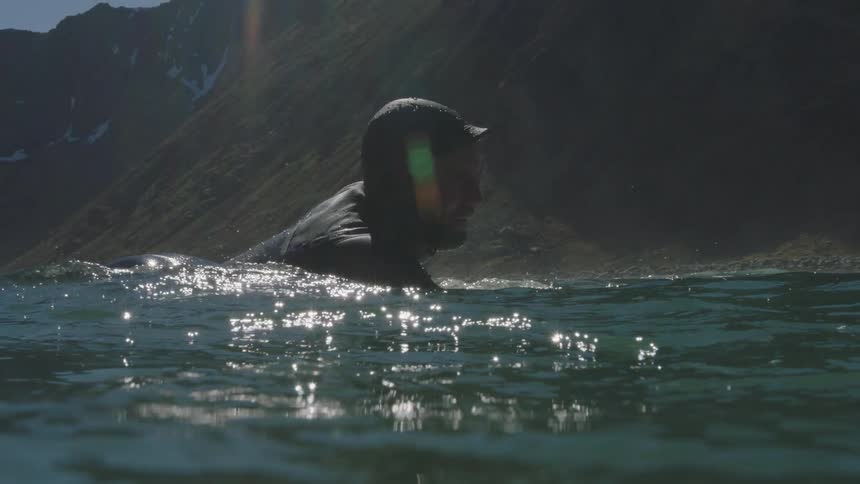 A surfer is paddling in ocean waters offshore on a cold day