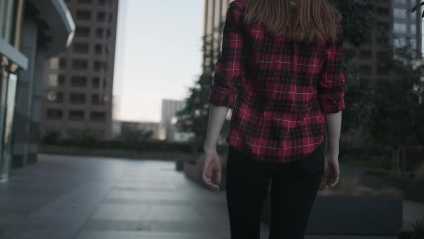 A woman in a flannel shirt walks near a glass building