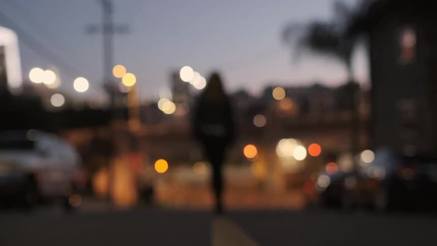 A woman is walking in the middle of a city street at dusk