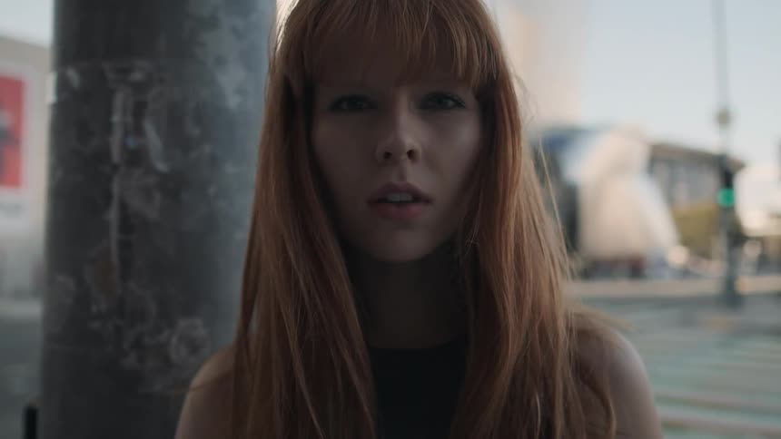 A red haired women stands and stares on a street corner
