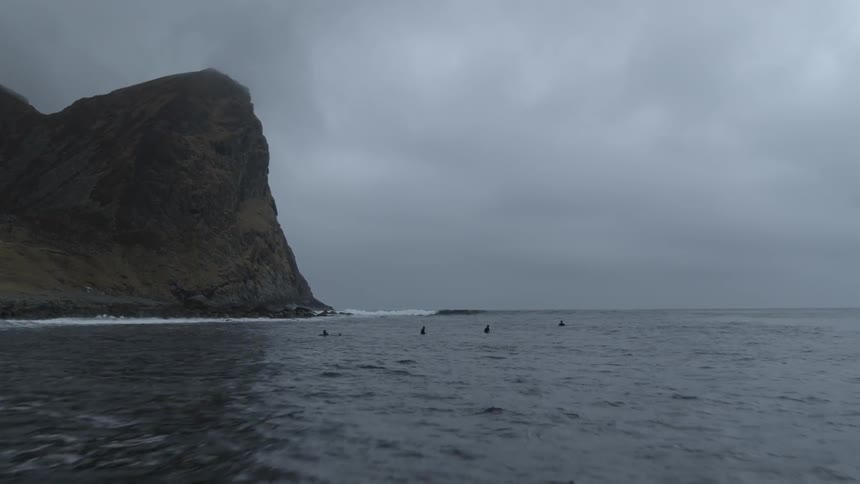 Surfers float in the water off a shoreline on a cloudy day